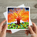 Colourful greeting card with a tree of life design held by hands on a wooden surface
