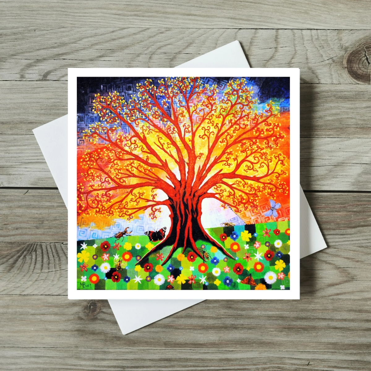 Colourful tree design on a greeting card with a white envelope on a wooden surface