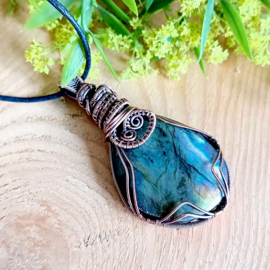 Blue stone pendant with copper wire wrapping on a wooden surface with greenery
