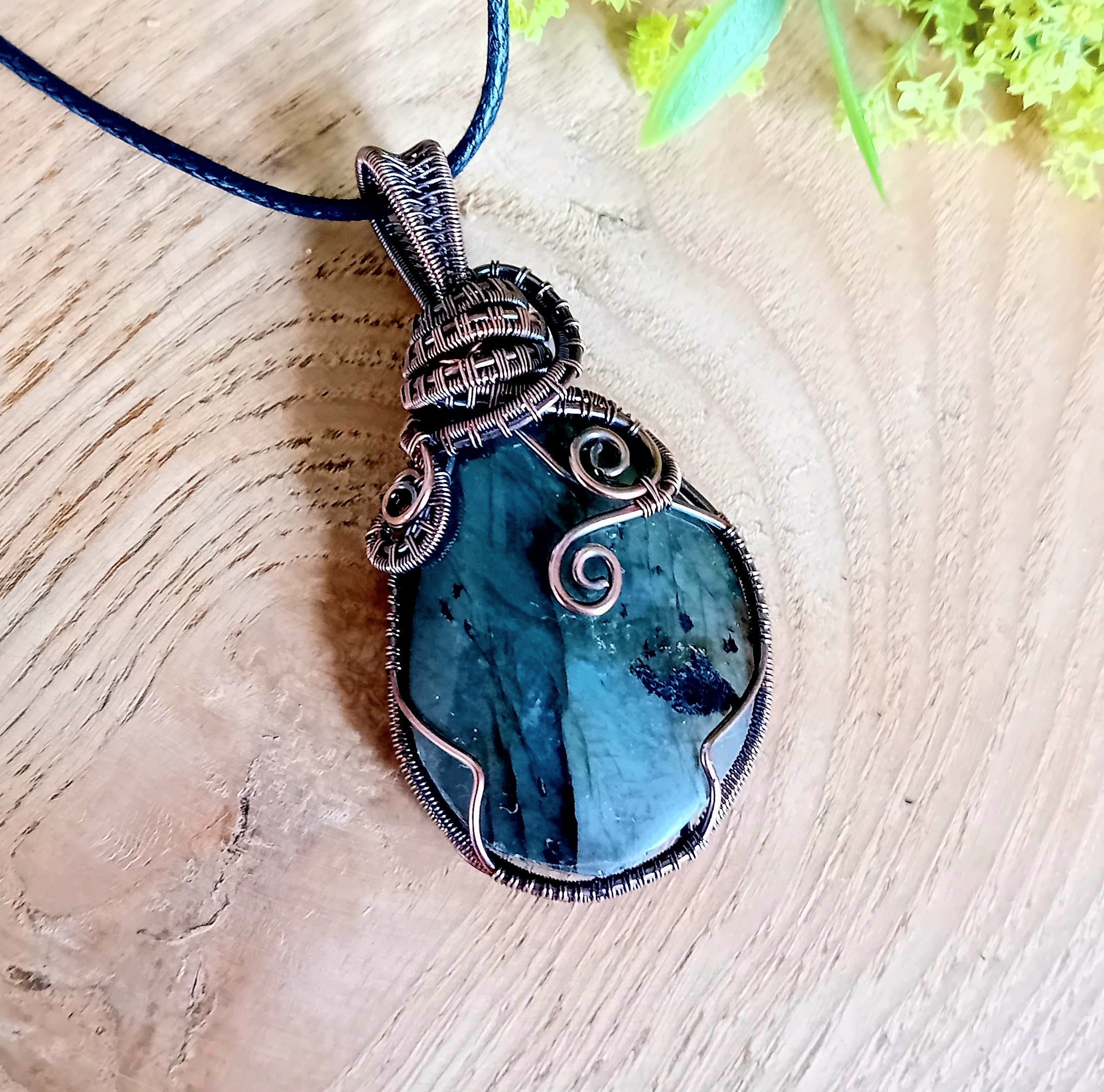 Blue pendant necklace on a wooden surface with green leaves