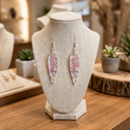 Floral feather-shaped earrings on a textured jewelry stand with a blurred background