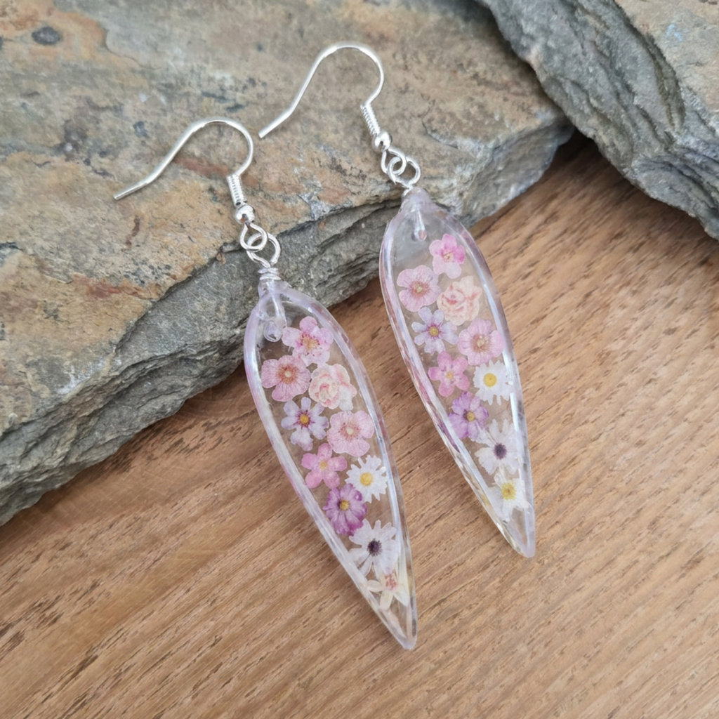 Translucent leaf-shaped earrings with floral design on a wooden surface.