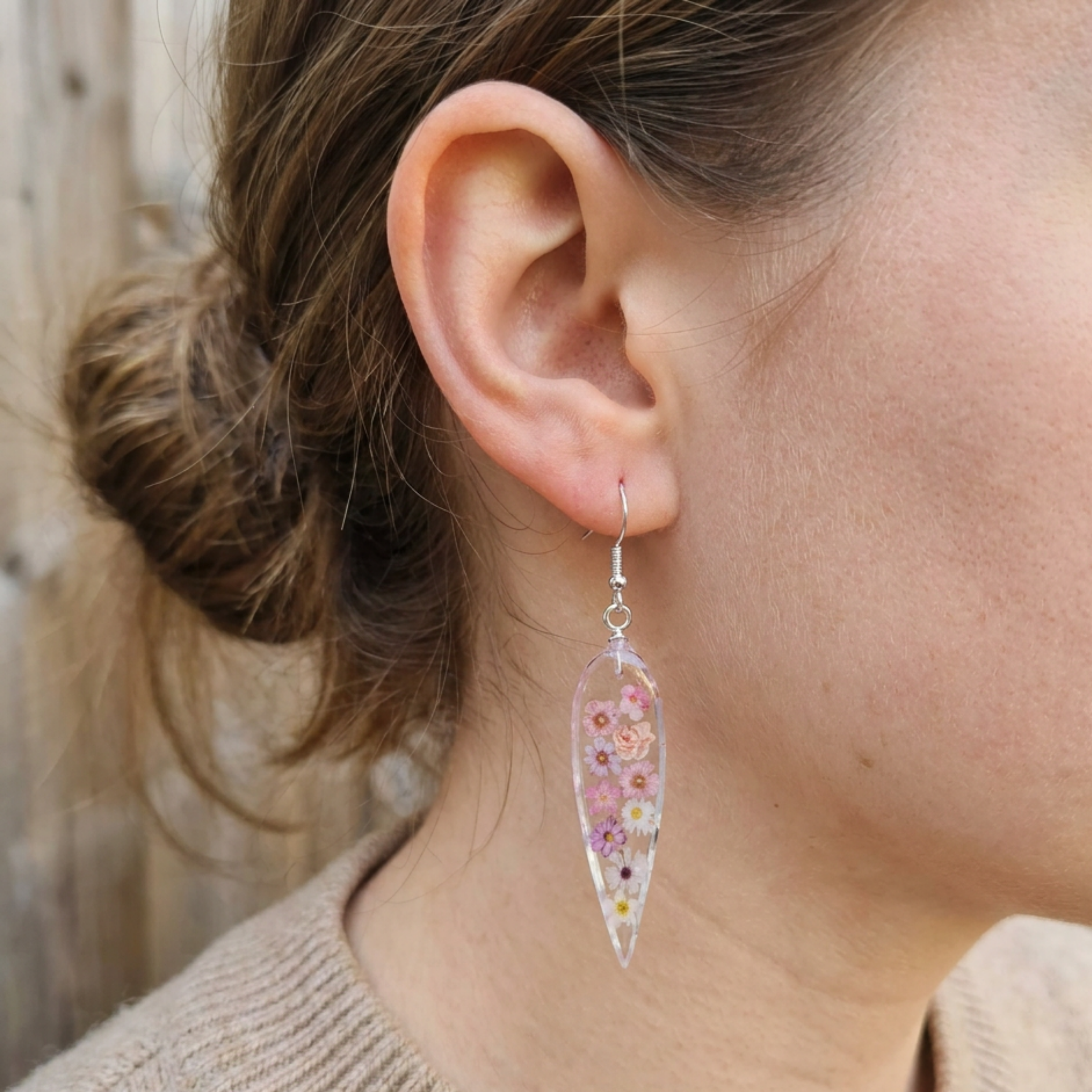 Teardrop-shaped earrings with floral design worn by a person.