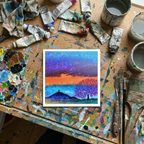 Artistic depiction of a landscape with a colourful sky and Glastonbury Tor on a paint-covered table with art supplies.