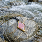 Diamond pendant with a pink suspended flower sitting on a rock in the river