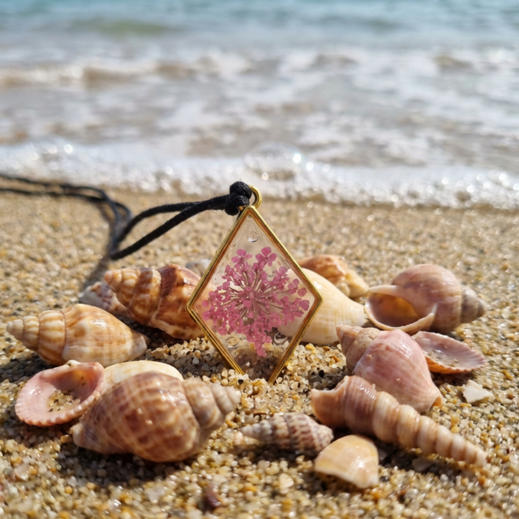 Necklace with a pink floral pendant on a sandy beach with shells.