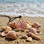 Necklace with a pink floral pendant on a sandy beach with shells.