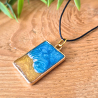 Rectangular pendant with blue and gold design on a wooden surface