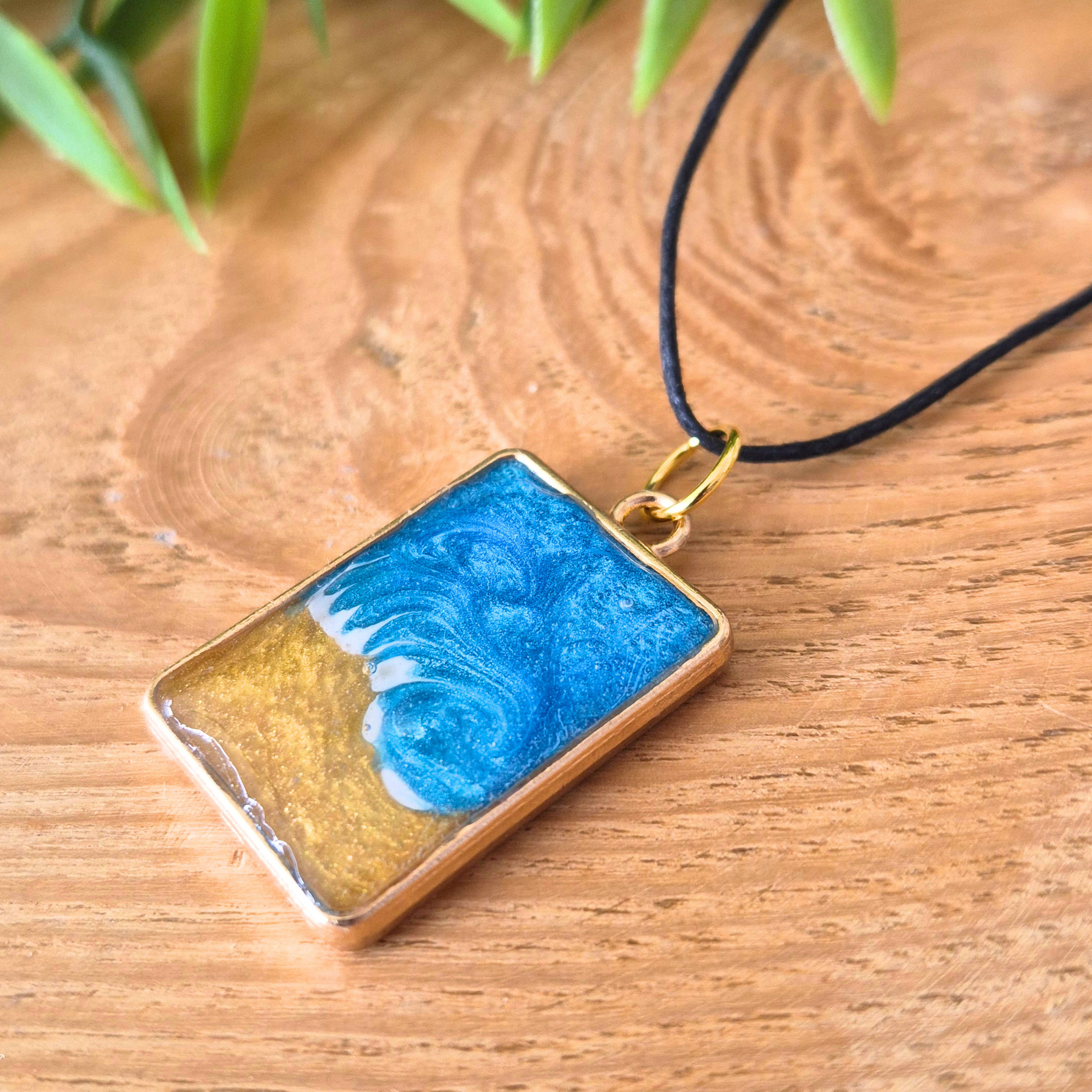 Rectangular pendant with blue and gold design on a wooden surface