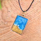 Rectangular pendant with blue and gold design on a wooden surface