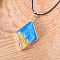 Striking wave pendant in a gold diamond bezel on a wooden surface