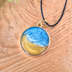 Round pendant with blue and gold design on a black cord, placed on a wooden surface.