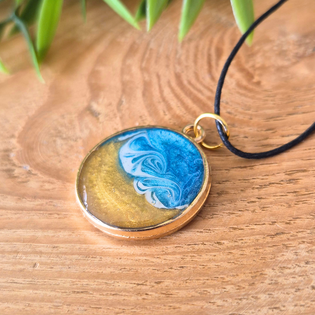Round pendant with blue and gold design on a wooden surface