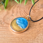 Round pendant with blue and gold design on a wooden surface