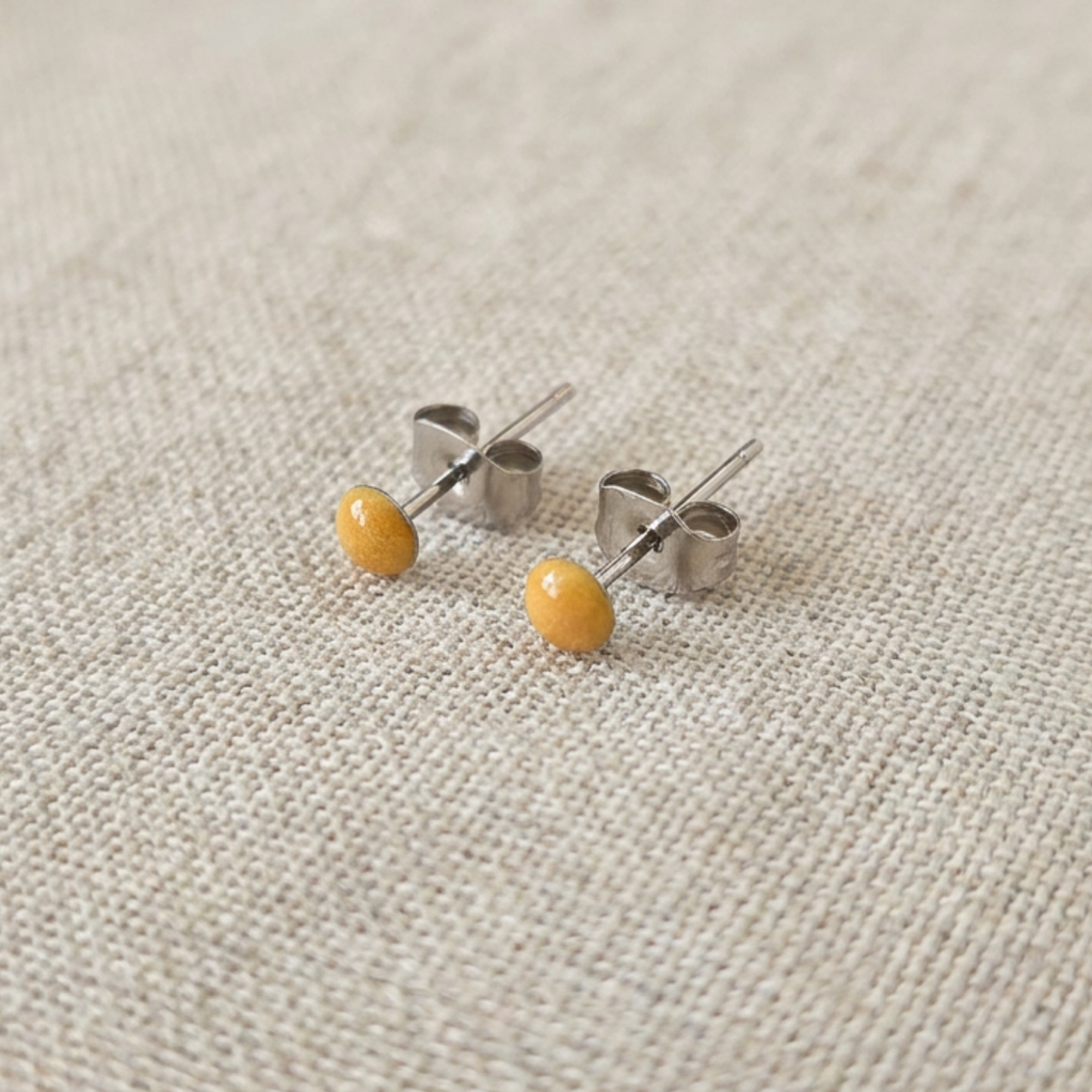 Pair of small earrings with yellow beads on a textured beige background