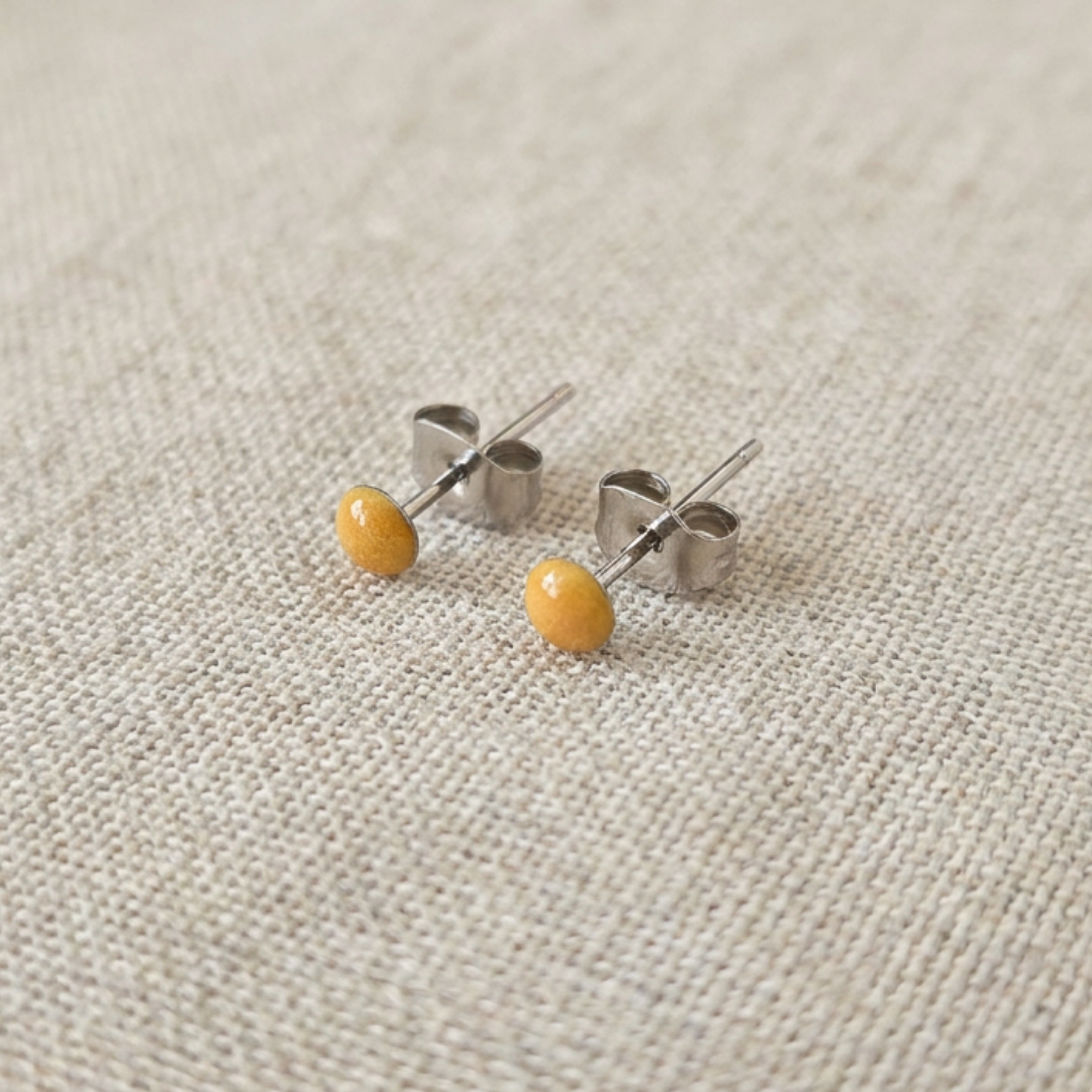 Pair of small earrings with yellow beads on a textured beige background