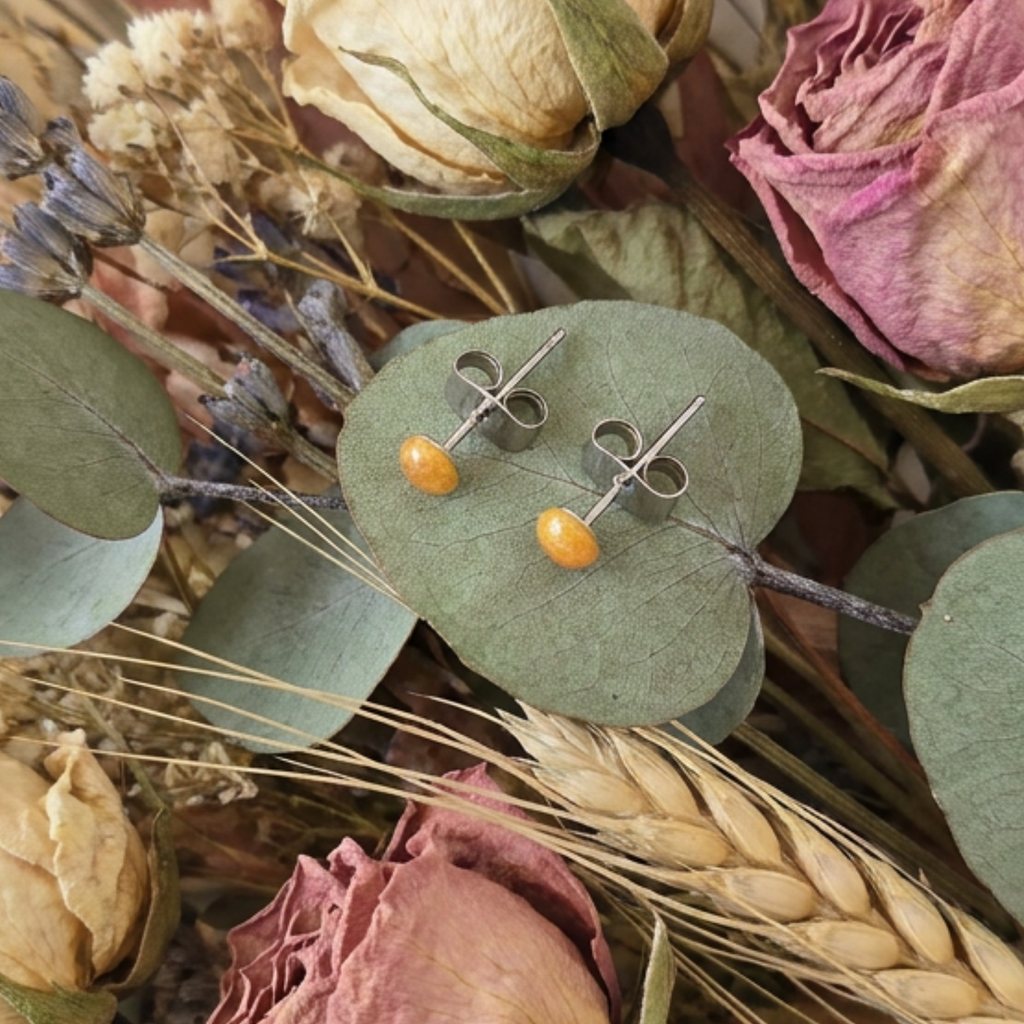 Pair of earrings with orange beads on green leaves surrounded by dried flowers and plants