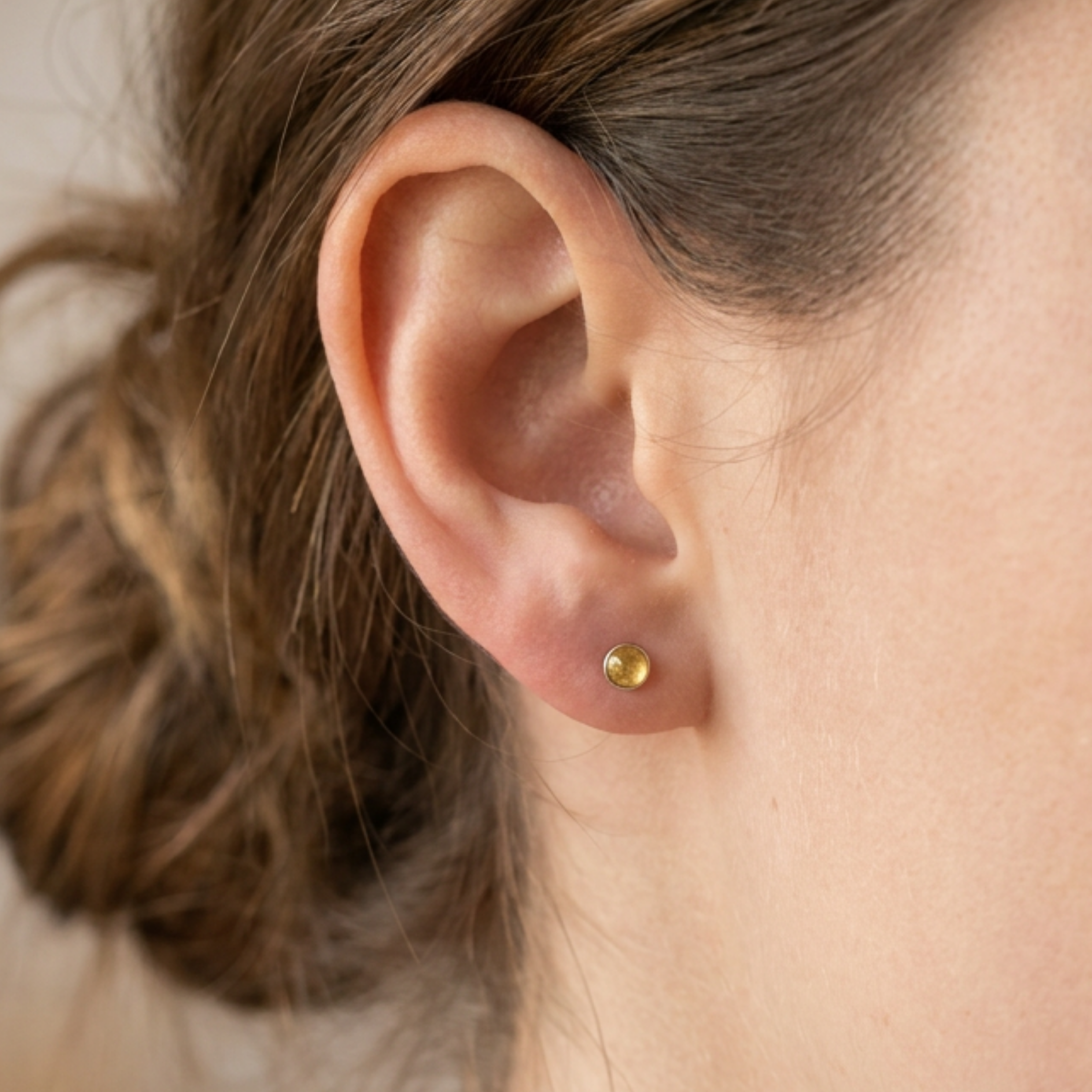 Close-up of an ear wearing a small round earring with a blurred background