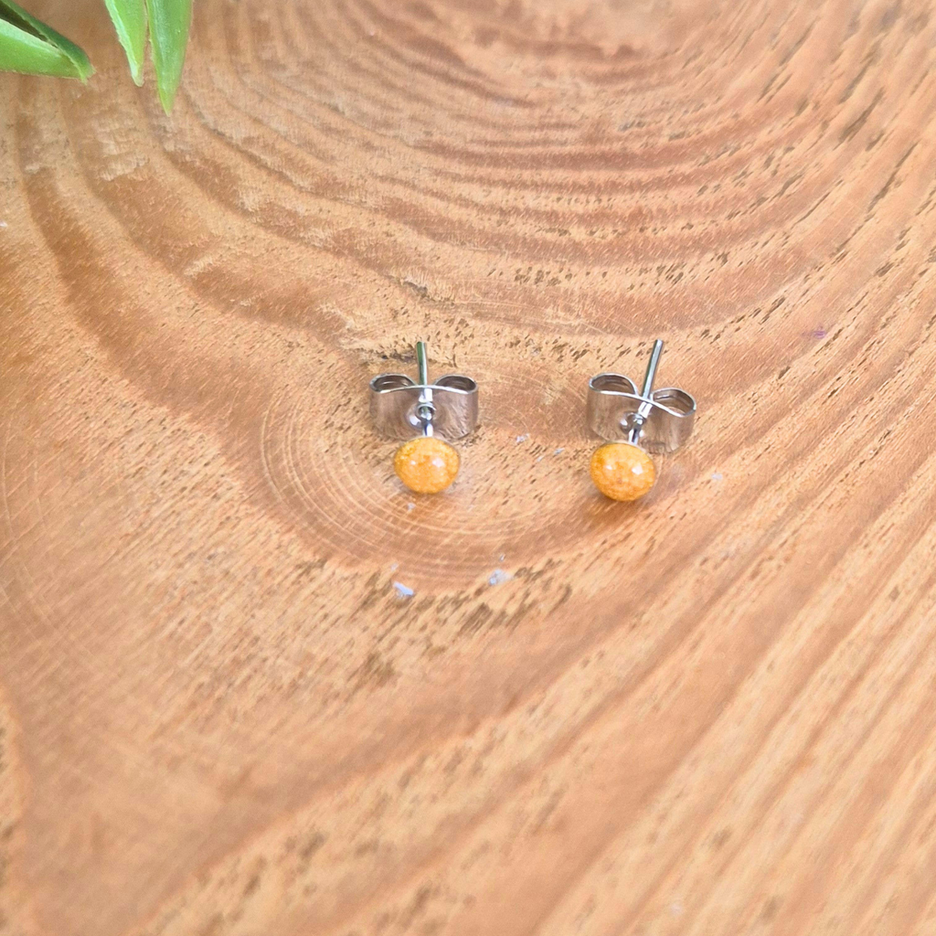 Pair of small orange stud earrings on a wooden surface
