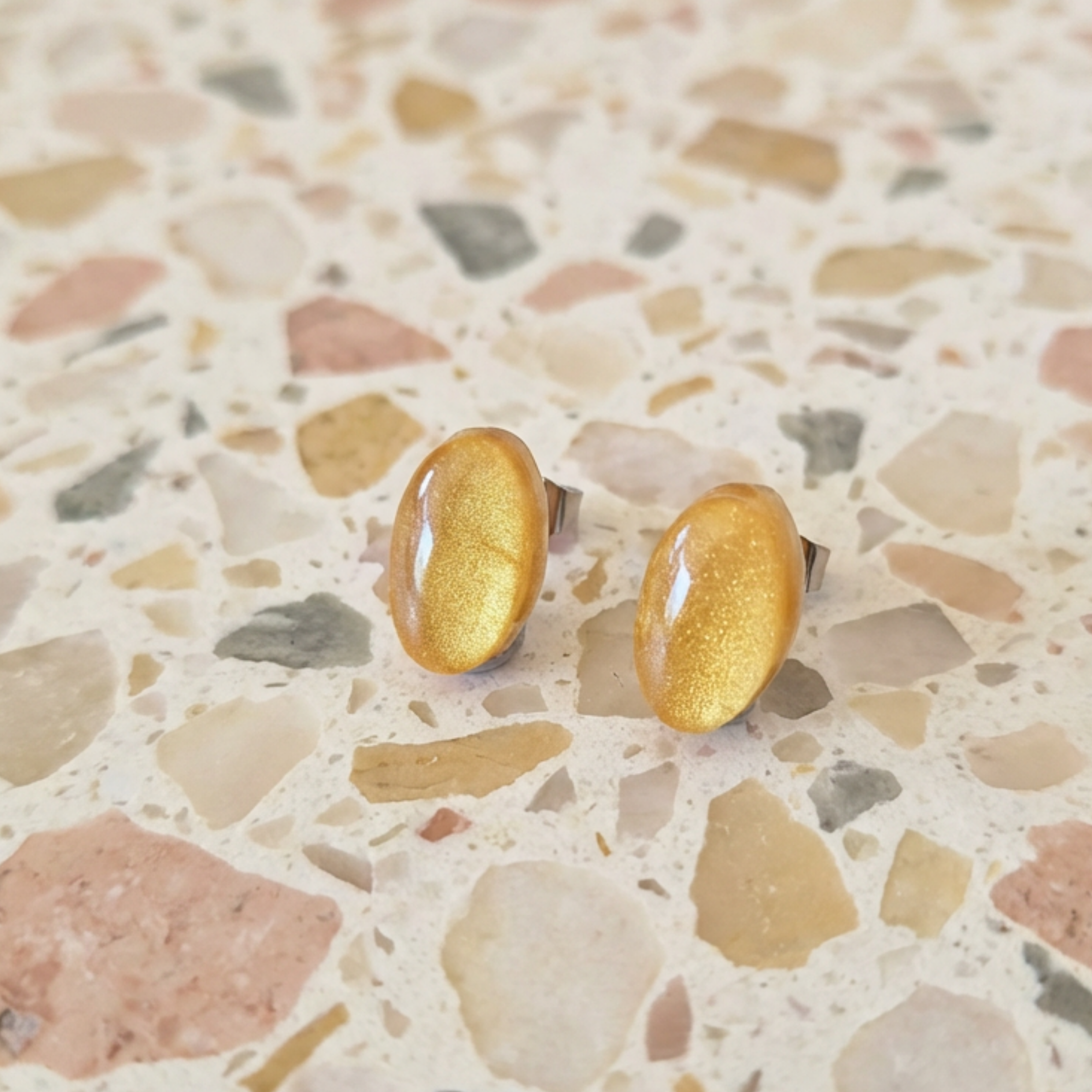 Gold shimmer oval earrings on a decorative surface