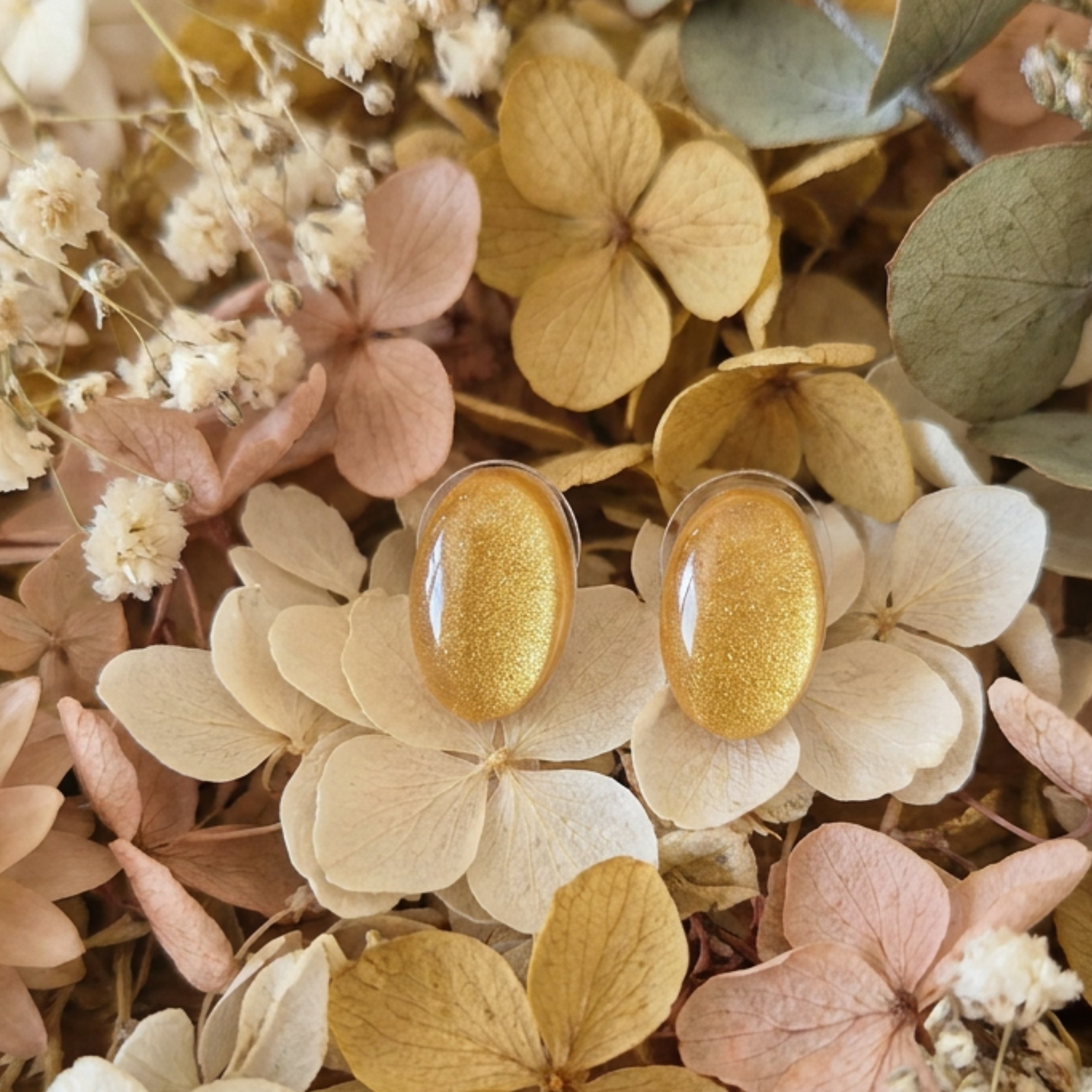 Gold oval earrings on a background of dried flowers