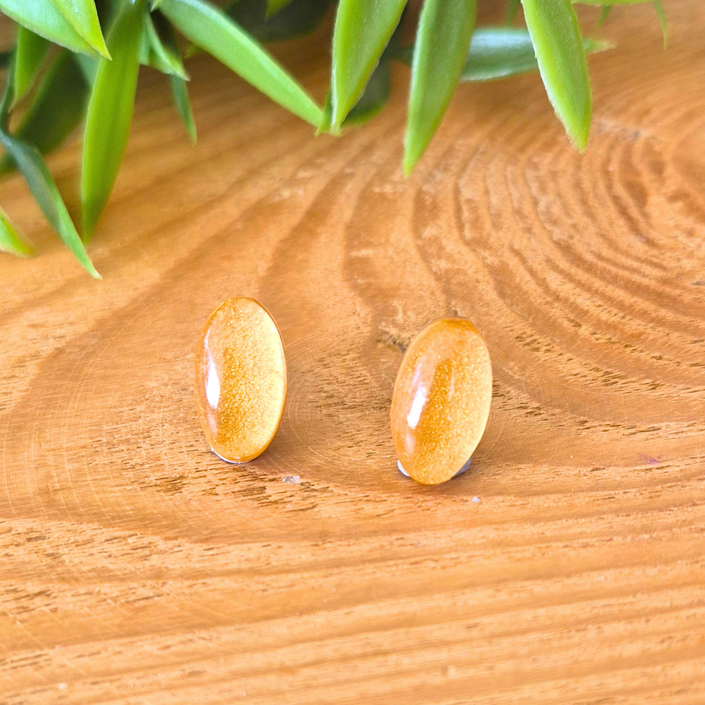 Gold oval stud earrings on a wooden surface