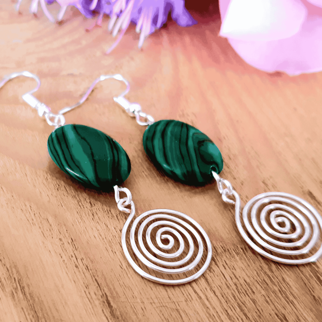 Earrings with green marbled stones and white spiral designs on a wooden surface.