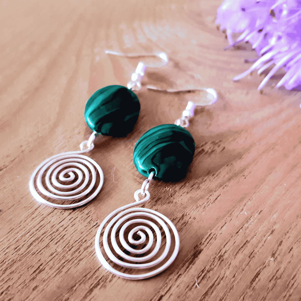 Green beaded earrings with silver spiral designs on a wooden surface