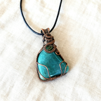 Green Aquamarine pendant with copper wire wrapping on a beige fabric background