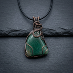 Green stone pendant with copper wire wrapping on a dark background