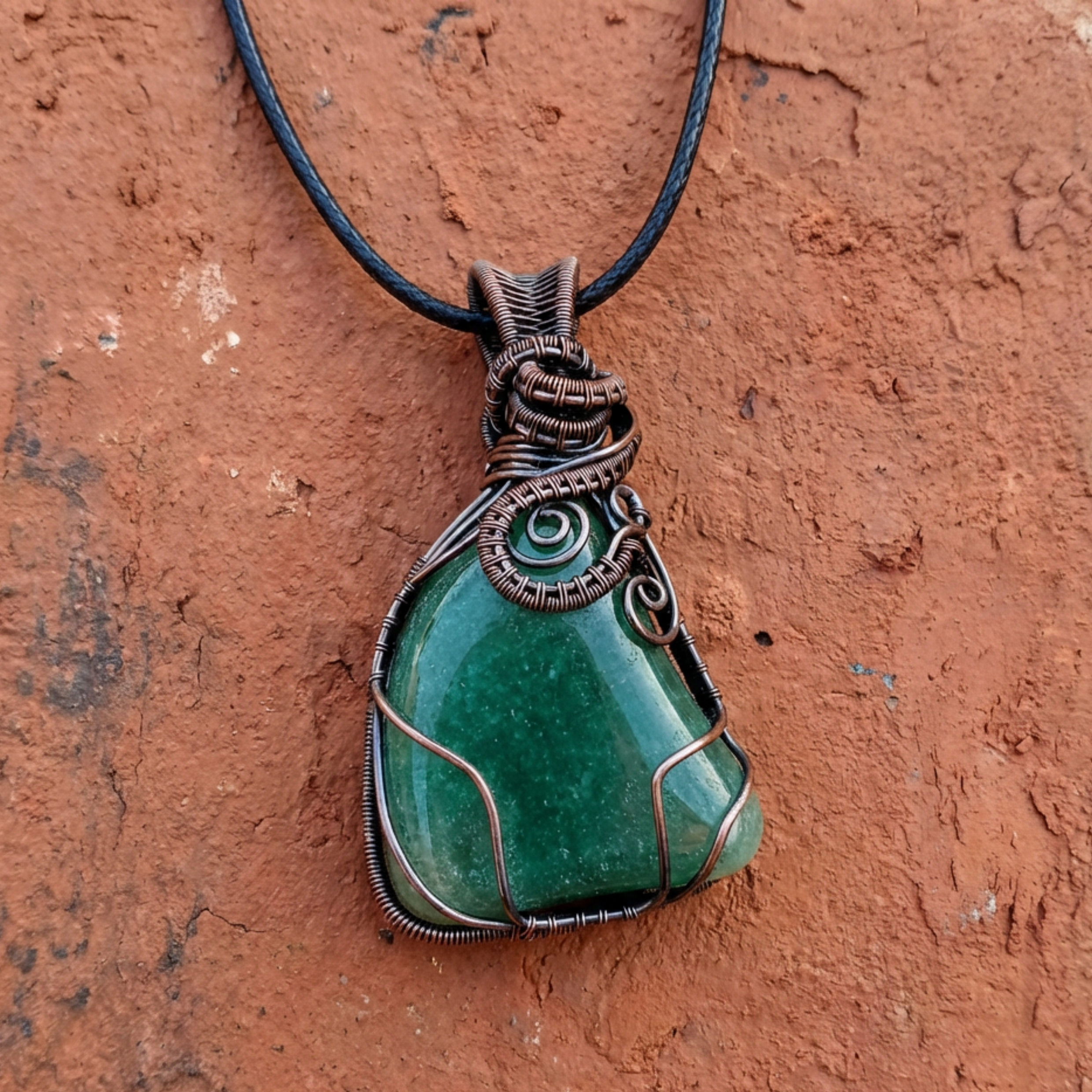 Green stone pendant with copper wire wrapping on a brown textured background