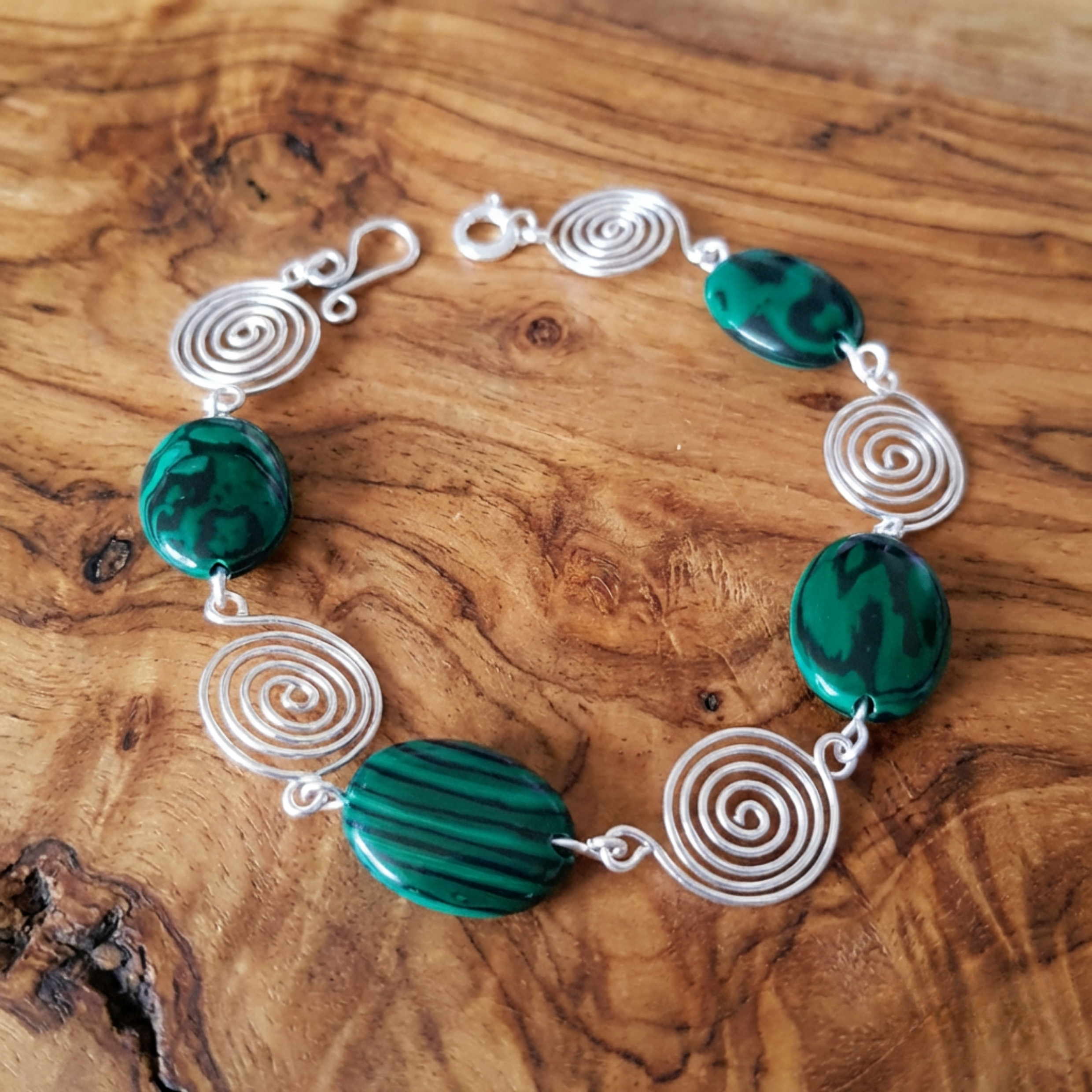 Bracelet with green beads and silver spiral designs on a wooden surface