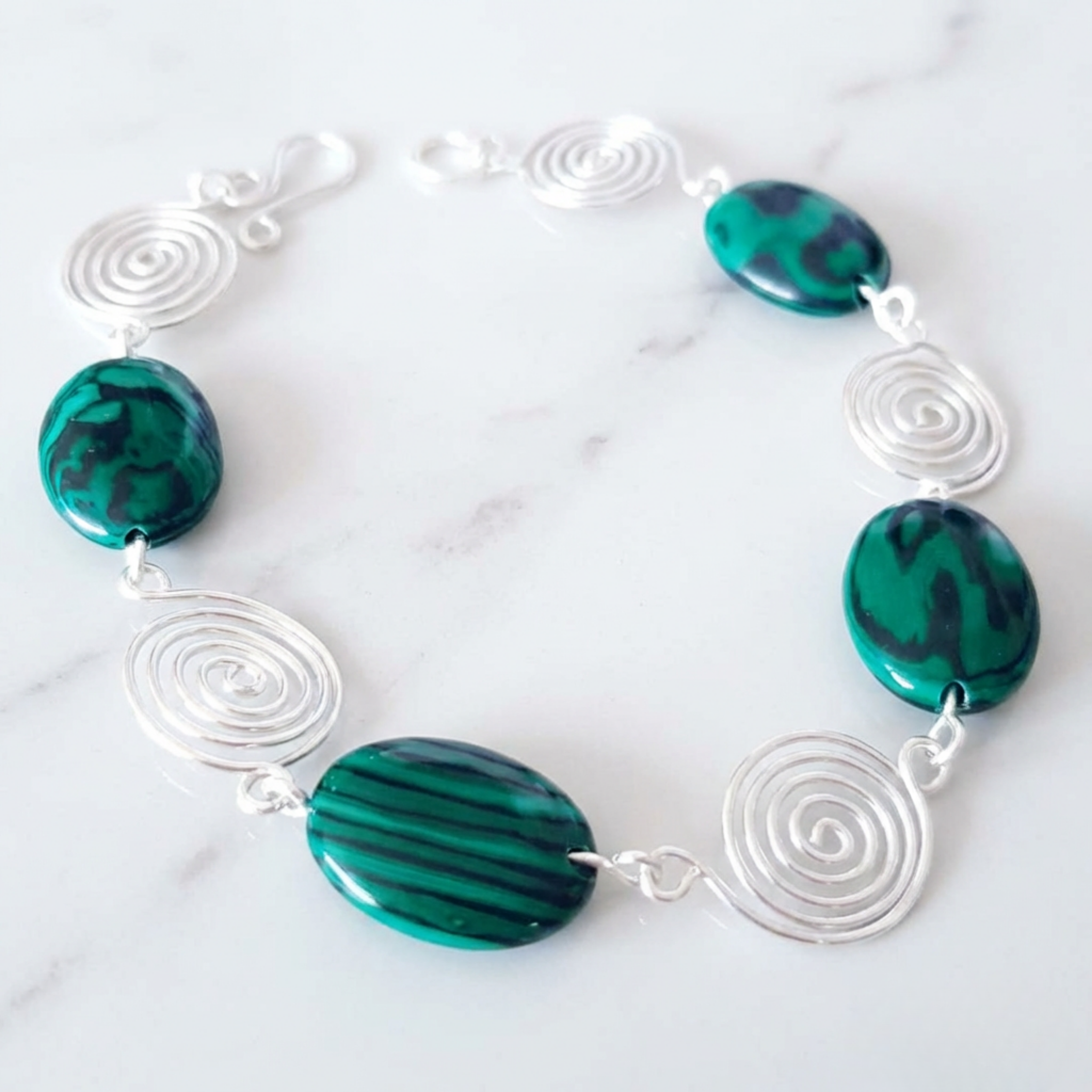 Bracelet with green marbled stones and silver spiral designs on a white marble background
