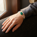 Hand wearing a bracelet with a green stone on a dark surface