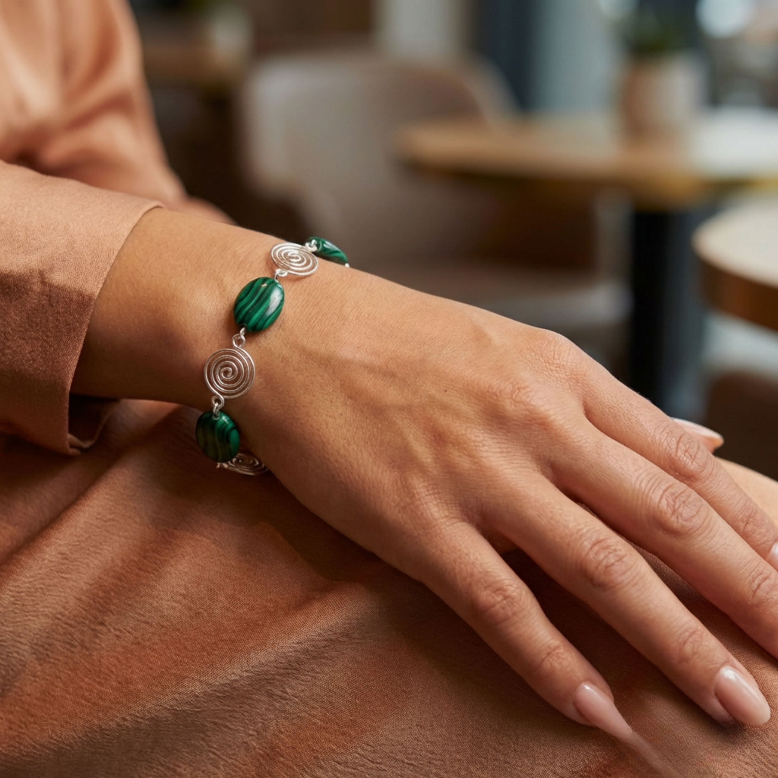 Close-up of a hand wearing a green beaded bracelet in a blurred indoor setting