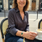Woman sitting outdoors with a cup of coffee, wearing a grey shirt and jeans and a silver spiral and green beaded bracelet