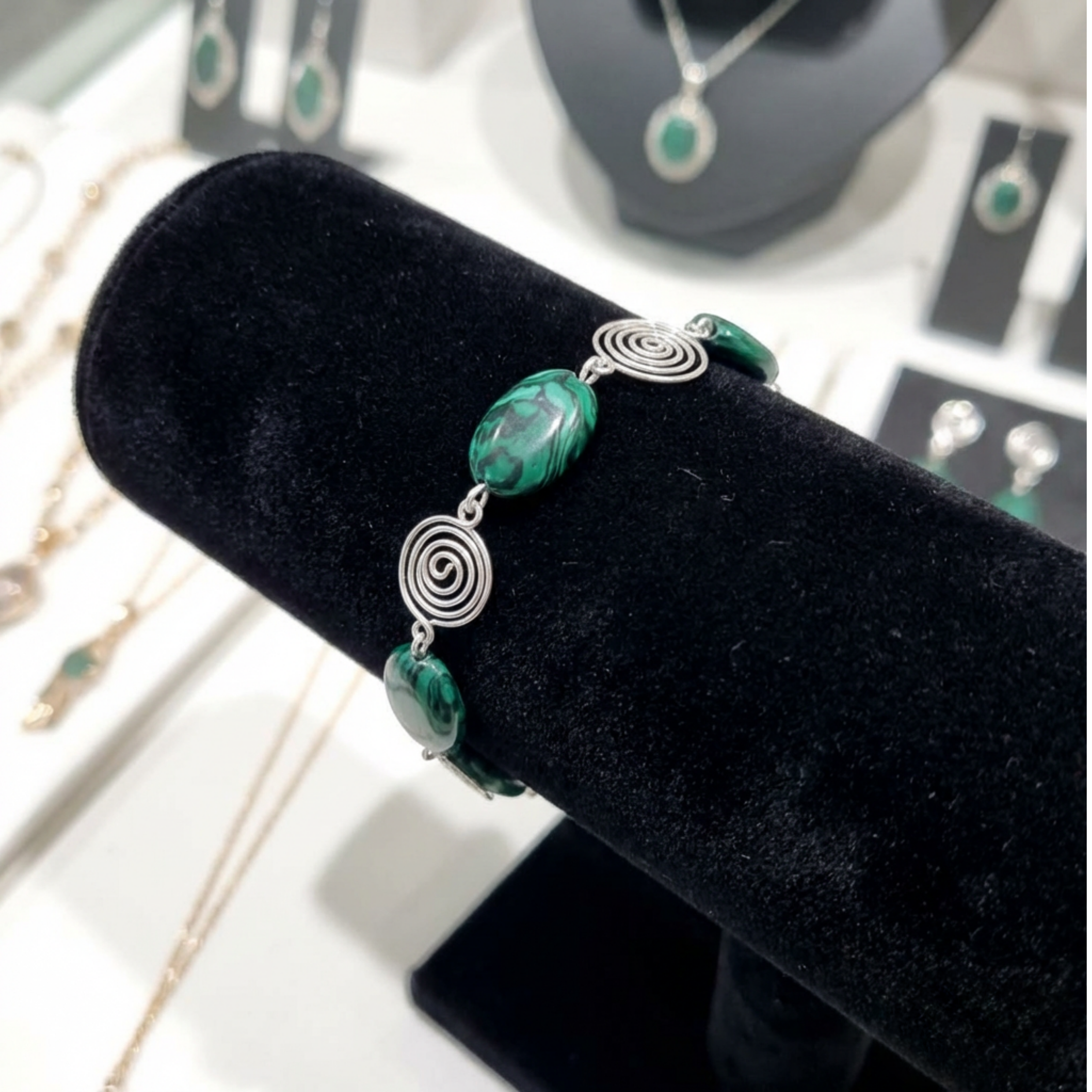 Green beaded bracelet with silver spirals on a black velvet stand with jewellery in the background