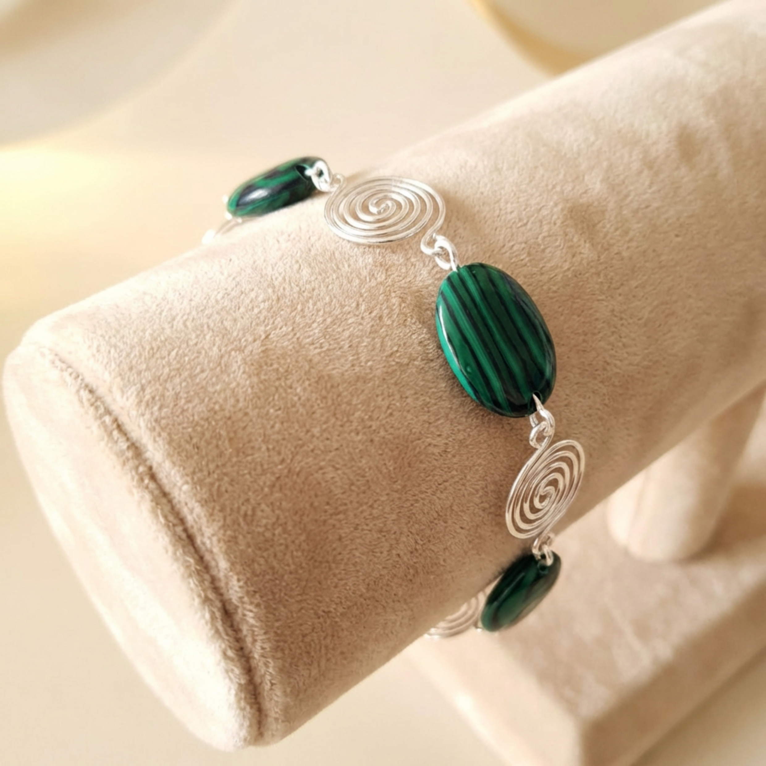 Bracelet with green beads and silver spiral designs on a beige cushion