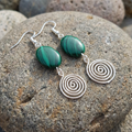 Green stone and silver spiral earrings on a textured stone surface