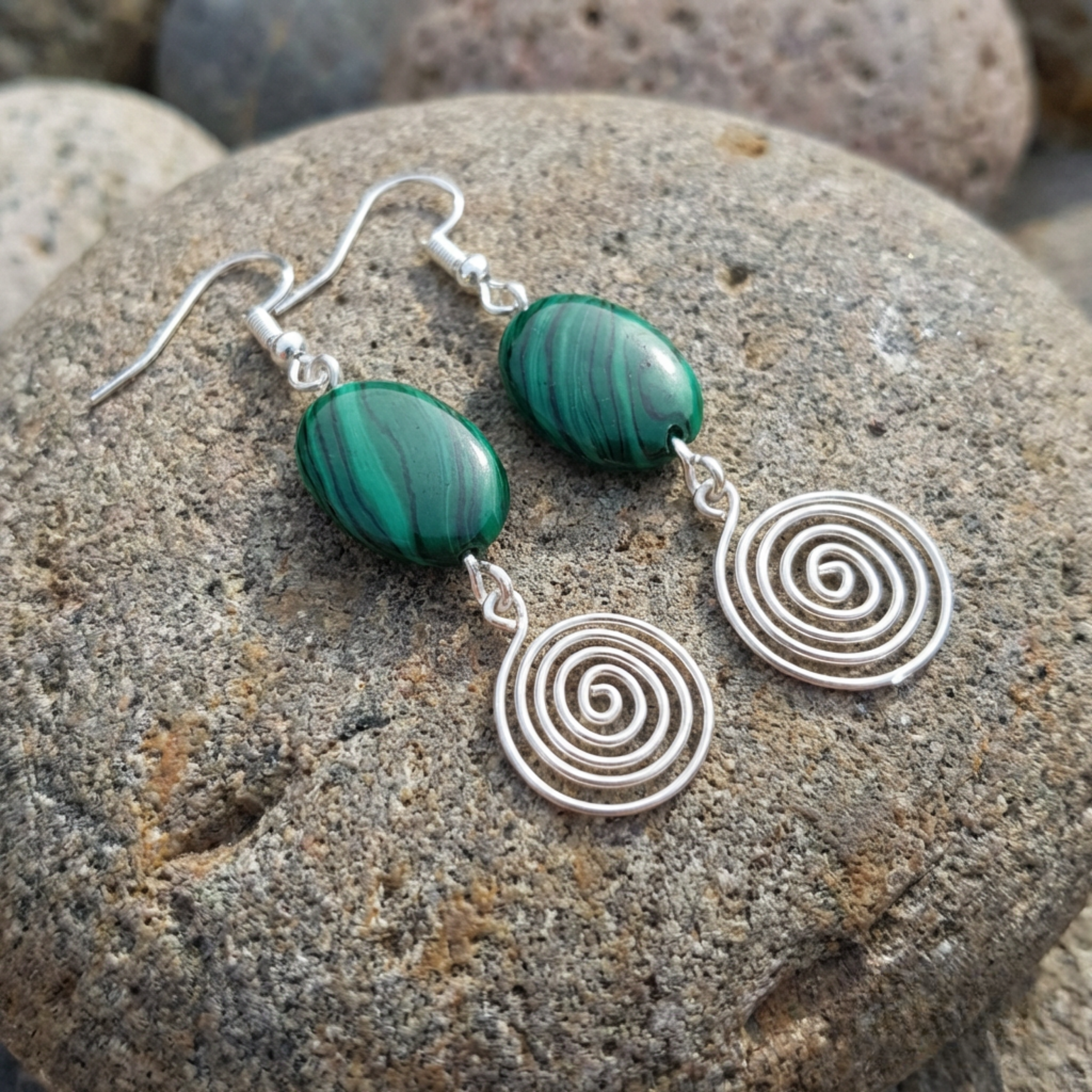 Green stone and silver spiral earrings on a textured stone surface