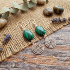 Pair of earrings with green stones and spiral design on a rustic wooden surface with burlap and lavender.