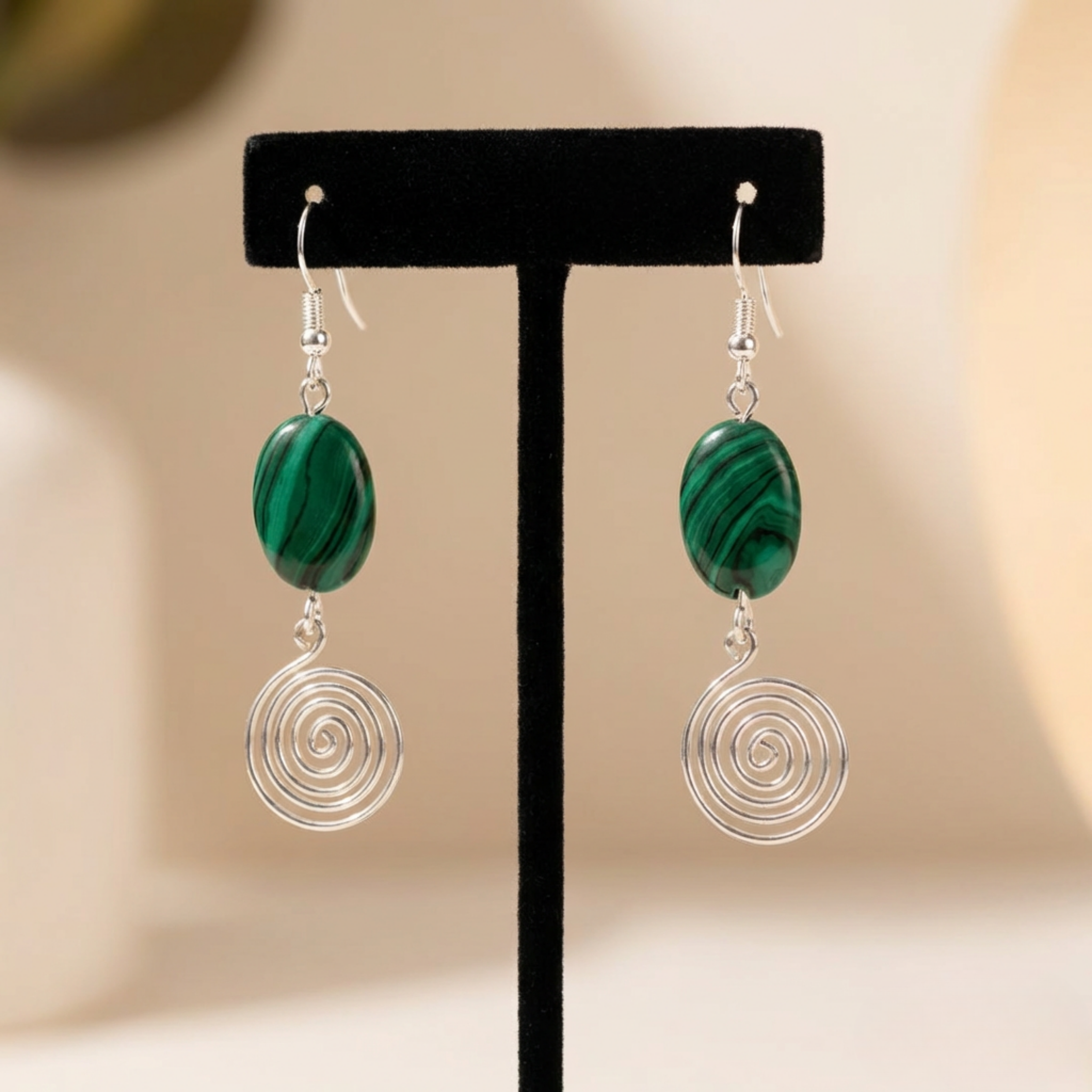 Pair of earrings with green marbled stones and silver spiral designs on a black stand.