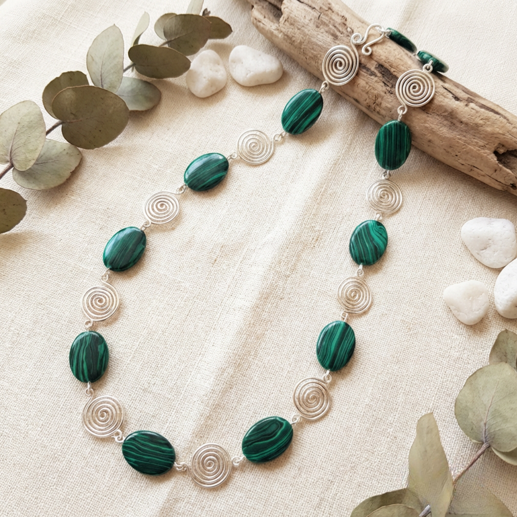 Necklace with green beads and silver spiral accents on a natural background with stones and leaves.
