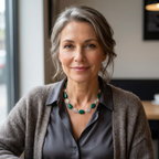 Woman wearing a grey cardigan and green necklace with silver spirals indoors