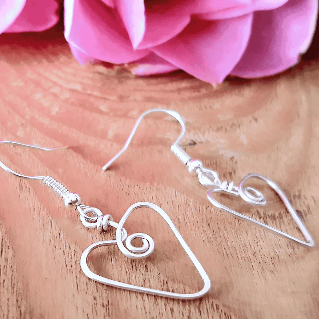 Silver heart-shaped earrings on a wooden surface with pink flowers in the background