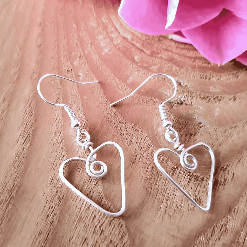 Silver heart-shaped wire earrings on a wooden surface with pink fabric in the background