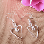 Silver heart-shaped wire earrings on a wooden surface with pink fabric in the background