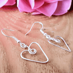 Silver heart-shaped wire earrings on a wooden surface with pink flowers in the background
