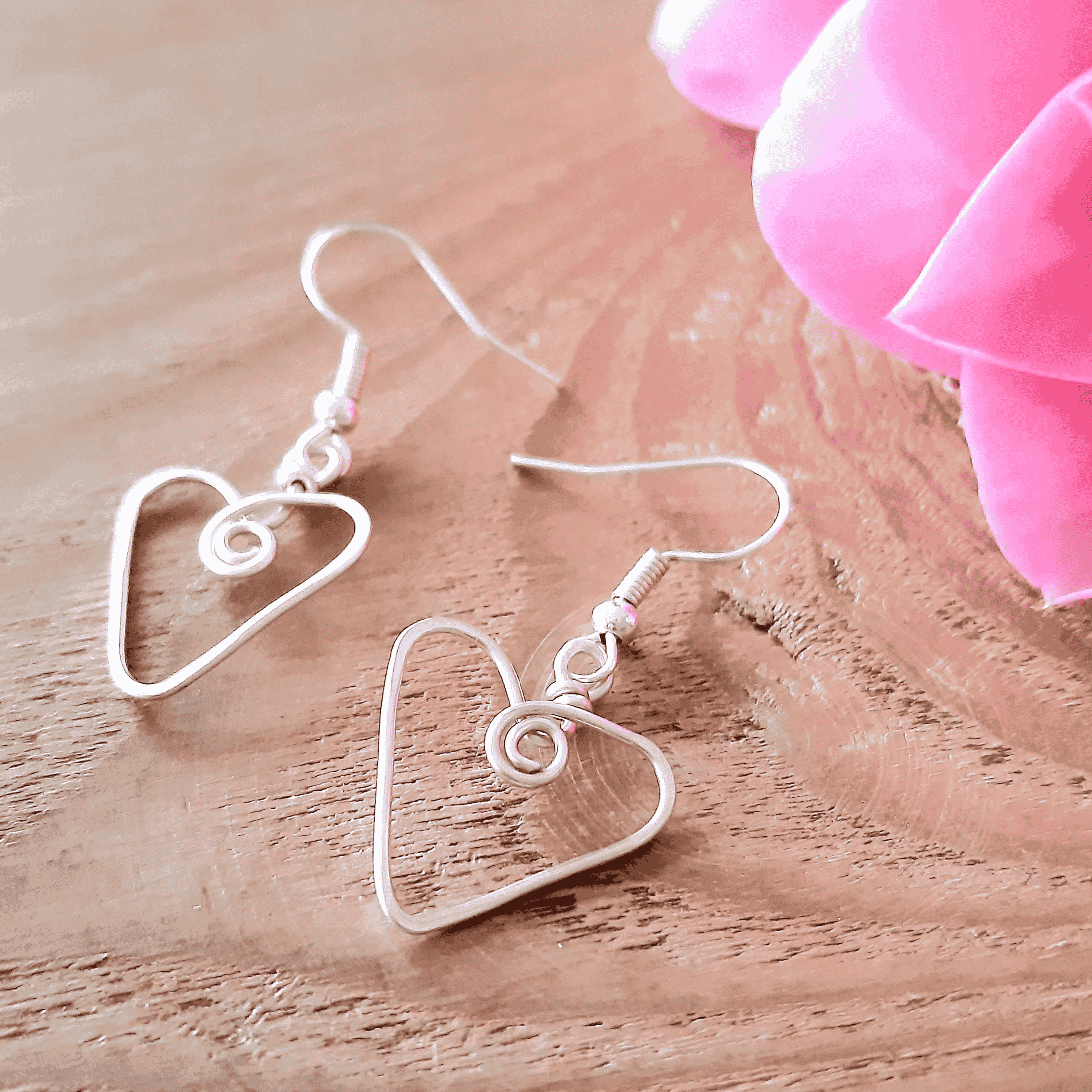Heart-shaped earrings on a wooden surface with pink fabric in the background