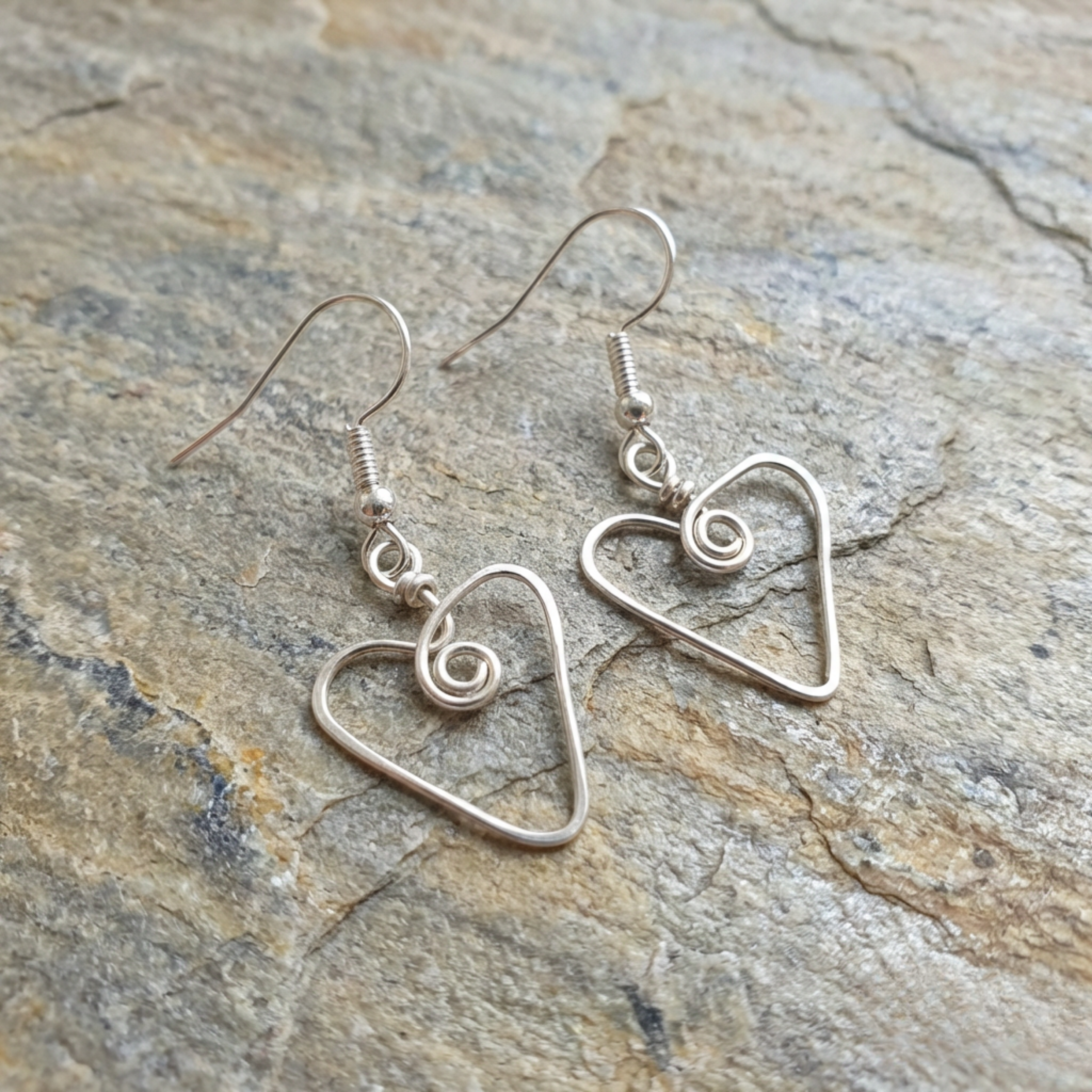 Silver heart-shaped earrings on a stone surface